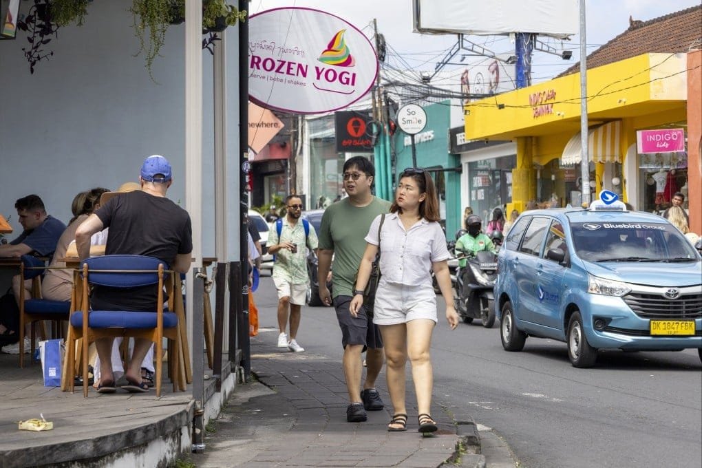 Tourists walking along a narrow sidewalk on a busy street in Bali, highlighting common first-time travel mistakes like unsafe walking and traffic awareness