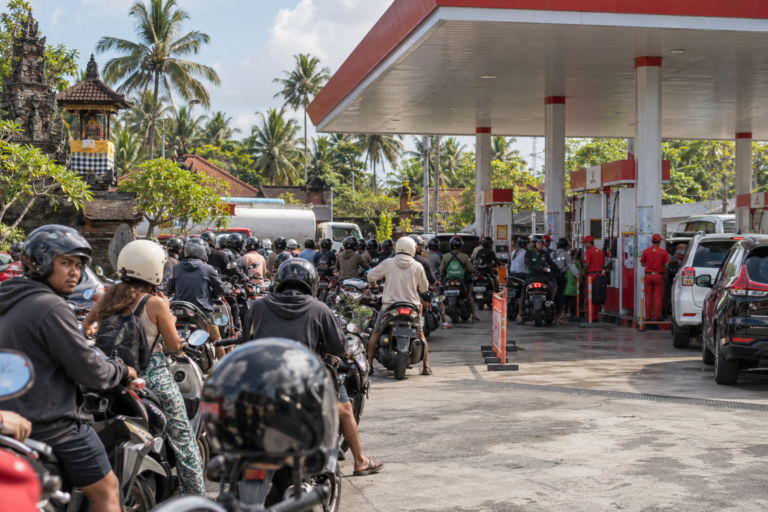 Illustration of a long queue of scooters and cars at a Bali gas station during the October 2026 fuel shortage.